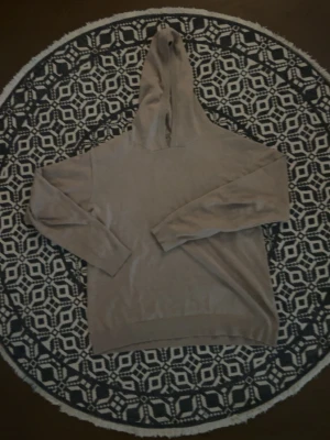 Beige hoodie med huva - En stilren beige hoodie med huva och långa ärmar. Hoodien har ribbade muddar vid ärmslut och nederkant. Perfekt för en avslappnad och enkel look. Materialet ser ut att vara mjukt och bekvämt.