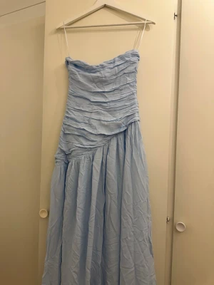 Ljusblå långklänning Adoore - Snygg ljusblå långklänning och draperad överdel. Klänningen har en asymmetrisk söm i midjan och ett luftigt, svepande tyg som ger en romantisk känsla. Perfekt för sommarens alla tillfällen. OBS liten defekt kolla på bilderna. Syns ej när man har på sig den, helt ny med prislapp!