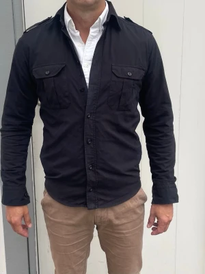 Svart overshirt från Eton - S - Jag säljer den här riktigt schyssta overshirten från Eton i storlek 38 vilket motsvarar S. Den är knappt använd och i mycket fint skick. Nypris låg på runt 2000kr och jag säljer den här för 599kr. Tveka inte att höra av er!