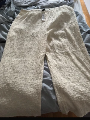 Byxor  - Säljer ett par vita byxor från Lindex i storlek XXL. Byxorna har en avslappnad passform med resår i midjan och ett krinklat tyg som ger en cool struktur. Perfekta för en chill och luftig stil. Helt nya med prislapp kvar!💕