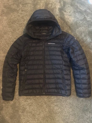 Tunn dunjacka med huva från peak performance  - Säljer en svart dunjacka med huva från Peak performance i extremt bra skick. Lättviktigt material och quiltad design gör den perfekt inför de lite kallare dagarna och till skolstarten. Fraktar samma dag plagget är köpt❤️‍🩹