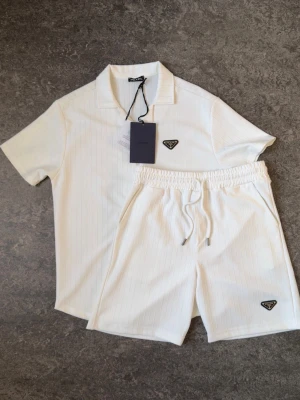 Vitt Prada set med skjorta och shorts - 👕 Plagg: Set med skjorta och shorts  📏 Storlek: S 🏷️ Märke/modell: Prada ✨ Skick: Fint skick, 8,5/10. Några mindre märken/fläckar som syns på bilderna, annars i nytt skick.  Vid frågor eller funderingar är det bara att skriva! Tveka inte på att lägga ett bud för bra business!🤝Kan även säljas separat om de behövs.
