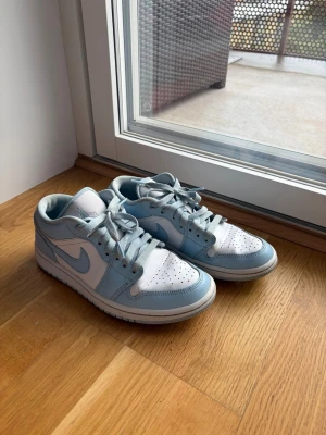 Nike ljusblå och vita sneakers - Säljer ett par fräscha Nike sneakers i ljusblått och vitt. Skorna har klassisk låg siluett, perforerad tåbox och ikoniska swoosh-loggan på sidan. Tillverkade i läder med matchande ljusblå snören och vit sula. Perfekta för dig som gillar stilrena och trendiga sneakers.               (Skosnören inte tvättade)