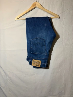 Blå jeans från Replay - Snygga blå jeans från Replay med klassisk femficksdesign och raka ben. Jeansen har en mellanblå tvätt och detaljerade sömmar på bakfickorna. Tillverkade i ett mjukt och stretchigt denimtyg för extra komfort. De hadde ett litet hål som jag sydde ihop, men kan säga att jag själv gått runt och man såg inget, pris kan diskuteras 