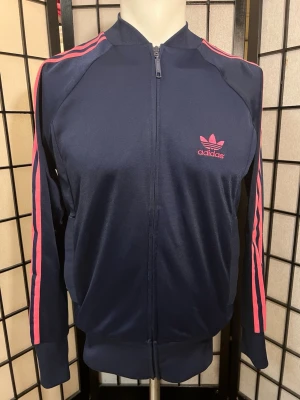 🔥 ADIDAS Y2K TRACK JACKET 2007 💗  - WOW!! 😍🔥 Ikonisk adidas Originals track jacket från 2007 i marinblått och knallrosa 💗💙  Broderad Trefoil, klassiska 3-Stripes och perfekt Y2K/00s retro-look! Mjuk insida och supersnygg figurnära passform – ett riktigt statement-piece till jeans, cargos eller tights ✨  🏷️ Storlek S 📏 P2P: 50–51 cm 📏 Längd: 58–59 cm ⭐ Mycket fint skick  Svår att hitta i den här färgen! 💎  📦 Snabb frakt 💬 Bud & bundles välkomnas