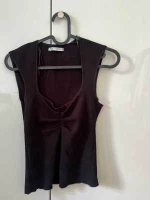 Topp från Zara - Säljer en populär svart ärmlös topp från Zara med detalj framtill.💕