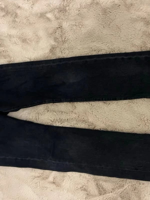 Svarta raka jeans från Levi's - Snygga svarta jeans från Levi's med klassisk femficksdesign och raka ben. Jeansen har en mörk tvätt och detaljer som läderpatch bak i midjan och röd Levi's-tagg på bakfickan. Perfekta för en stilren och avslappnad look.