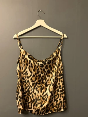 Leopardmönstrat linne  - Säljer ett trendigt linne med leopardmönster och tunna axelband. Toppen har en lös passform och ett glansigt material. 