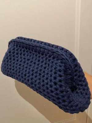 Handvirkad mörkblå clutch väska - Snygg mörkblå kuvertväska i virkat material. Väskan har en mjuk och flexibel form som är virkad av mig! Perfekt att bära i handen för en stilren touch till din outfit. KAN PRUTAS