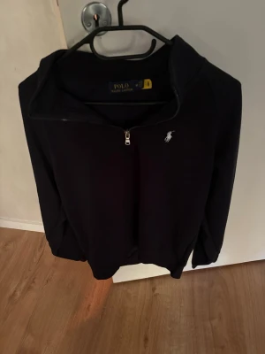 Mörkblå half-zip hoodie Polo Ralph Lauren - Snygg mörkblå hoodie från Polo Ralph Lauren med half-zip dragkedja och klassiska loggan broderad på bröstet. Tillverkad i mjukt bomullsmaterial och har en avslappnad passform. Perfekt för en casual och stilren look.