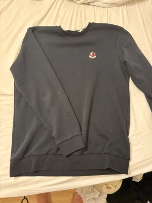 Moncler tröja  - Snygg mörkblå sweatshirt från Moncler med rund halsringning och broderad logga på bröstet. Tröjan har ribbade muddar vid ärmslut och nederkant, perfekt för en stilren och avslappnad look. Storlek L men kan också passa till M 