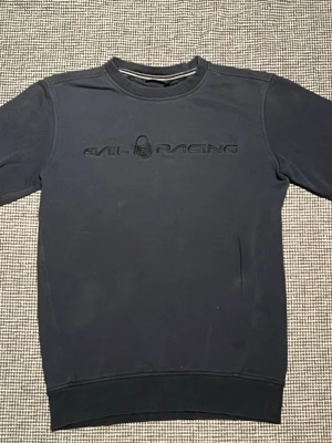 Marinblå Sail Racing sweatshirt - Snygg marinblå sweatshirt från Sail Racing med broderad logga på bröstet. Tröjan har rund halsringning, ribbade muddar och är tillverkad i mjukt bomullsmaterial. Perfekt för en avslappnad och stilren look.