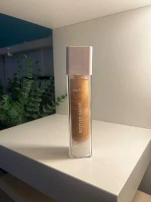 Bottled Glow highlighter i guld - Flytande highlighter från Technic i nyansen Bottled Glow. Kommer i en genomskinlig fyrkantig plastflaska med vit kork. Ger en intensiv gyllene glow och är enkel att applicera för en strålande finish.