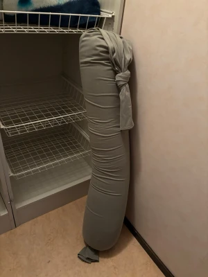 Grå gravidkudde från bbhugme - Lång, mjuk gravidkudde i grått tyg från bbhugme. Kudden har en avlång form och är försedd med knytband i ena änden för enkel justering. Perfekt för extra stöd och komfort vid vila eller sömn.
