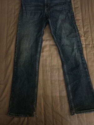 Mörkblå raka replay jeans - Säljer ett par mörkblå jeans med rak passform och klassisk femficksdesign. Jeansen har slitningar och ljusare partier framtill för en avslappnad look. Materialet är denim i bomull och benen är hellånga.