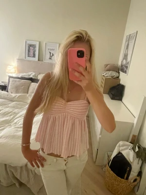 Ljusrosa randig topp - Supersöt ljusrosa linnetopp med vita ränder och tunna axelband. Toppen har en lätt rynkad byst och ett flowy fall som ger en luftig känsla. Perfekt för varma dagar och enkel att styla med jeans eller kjol.