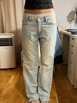 Ljusblå raka jeans med hög midja - Säljer ett par ljusblå jeans med rak passform och hög midja. Jeansen har klassiska fem fickor, knappgylf och en snygg tvättad look med slitningar framtill. Perfekta för en avslappnad och trendig stil.