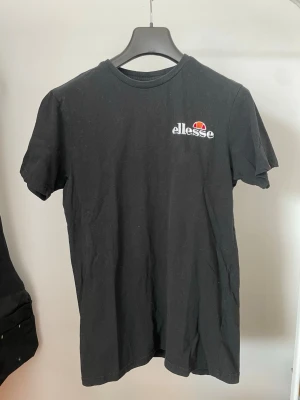 Svart t-shirt från Ellesse - Säljer en svart t-shirt från Ellesse med klassisk logga tryckt på bröstet. T-shirten har rund halsringning och korta ärmar. Perfekt basplagg med enkel och stilren design.