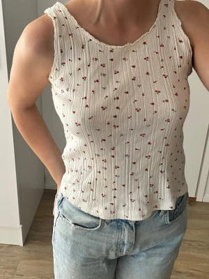 Vit ribbad linnetopp med små blommor - Söt vit ribbat linne med små röda blommor. Köpt på Zaras barn avdelning men passar mig som vanligtvis har storkek S, stretchig passform som sitter snyggt på kroppen.