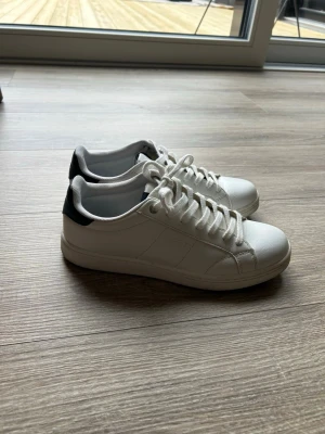 Vita Björn Borg sneakers - Fräscha vita sneakers från BORG med svart detalj på hälen och klassisk låg profil. Skorna har vita snören och ovandel i slätt material som ger en clean look. Perfekta för dig som gillar stilrena och tidlösa sneakers. Endast använda 2 gånger, säljer dem för att dem är alldeles för små för mig.