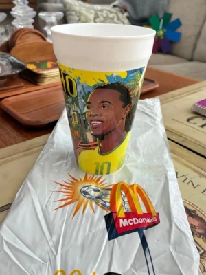 McDonald's samlarmugg fotboll - Cool samlarmugg från McDonald's med färgglad illustration av en fotbollsspelare i gul tröja och nummer 10. Muggen har vita kanter och motivet är tryckt i starka färger. Perfekt för dig som gillar sport eller samlar på unika muggar.