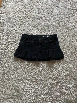 Svart volangkjol  - En Lågmidjad svart jeanskjol omsydd från ett par jeans.   Midjemått tvärsöver - ca 42cm Längd - ca 29cm