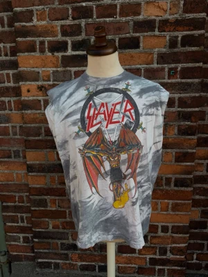 Slayer Crucified Demon Tie Dye 1988 – Original Vintage XL - Original Slayer Crucified Demon från 1988 med klassiskt tie-dye-mönster och stort demonmotiv framtill. Märkt Fruit of the Loom XL, tillverkad i Irland och med ©1988 Slayer i trycket. Ett eftertraktat original från South of Heaven-eran.   Information  * Storlek: XL * Armhåla–armhåla: 60cm * Längd: 73cm * Fruit of the Loom * Made in Ireland * 100 % bomull