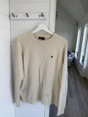 Morris Beige stickad tröja med brodyr - Säljer en stilren beige stickad tröja med rund halsringning och diskret broderad detalj på bröstet. Tröjan har långa ärmar och ribbade muddar vid ärmslut och nederkant. Perfekt för lager på lager och enkel att matcha. Nypris 2000+