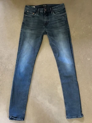 Blå slim fit jeans med slitningar - Snygga blå slim fit jeans med lätt slitna detaljer och klassisk femficksdesign. Jeansen har en något tvättad look och smala ben. Perfekta för en avslappnad och trendig stil. Materialet är troligtvis bomull med stretch för extra komfort. Jeansen är ifrån jack&jones och har storleken 30/34 men sitter som 29/32
