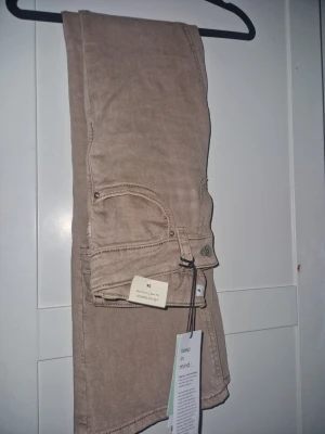 Beige bootcut jeans i storlek 36 - Ultra low waist y2k heter de! Säljer ett par snygga beige bootcut jeans i storlek 36. Jeansen har klassisk femficksdesign, bälteshällor och knappgylf. Perfekta för dig som gillar en avslappnad men trendig look. Materialet känns mjukt och följsamt. köpte de online och trodde jag var en storlek 36 men har 39 istället helt nya köptes 26 juli fick hem dem idag 28 juli helt nya!! Pris kan diskuteras formar kroppen fint helt nya!!!