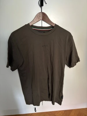 Olivgrön t-shirt från Replay - Snygg olivgrön t-shirt från Replay med diskret logga på bröstet. Klassisk rund halsringning och korta ärmar. Tillverkad i mjuk bomull som känns skön mot huden. Perfekt till jeans eller shorts för en avslappnad look.