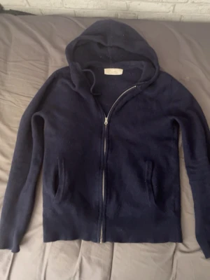 Mörkblå Kashmir tröja - Mysig mörkblå hoodie från Sayless i mjuk cashmere. Tröjan har dragkedja framtill, två fickor och en stor huva. Perfekt för dig som gillar stilrena och bekväma plagg med en lyxig känsla. Passar till det mesta och är enkel att matcha.