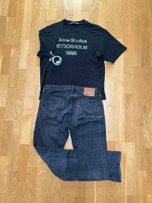 Levis 501 svarta jeans - Klassiska Levi's 501 jeans i svart tvätt med raka ben och femficksmodell. Jeansen har en snygg vintage-look och är tillverkade i bomull. Perfekta för dig som gillar tidlös stil och vill ha ett par jeans som funkar till allt.