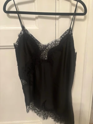 Ny viral Zara linne - Snygg svart linnetopp med tunna axelband och vacker spetsdetalj längs urringning och nederkant. Toppen har en mjuk, följsam känsla och ger en elegant look. Perfekt för att styla lager på lager eller bära som den är för en chic vibe.