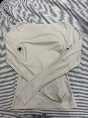 Ljusbeige långärmad topp från HM - En enkel och stilren ljusbeige långärmad topp med rund halsringning. Toppen har en slim passform och är tillverkad i ett mjukt, stretchigt material som känns skönt mot huden. Perfekt att matcha med jeans eller kjol för en clean look.