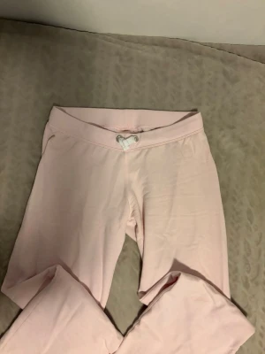 Ljusrosa mjukisbyxor från Gina Tricot - Säljer ett par ljusrosa mjukisbyxor från Gina Tricot med bred resår i midjan och vit dragsko framtill. Byxorna är raka i modellen och gjorda i mjukt bomullsmaterial, perfekta för chill dagar hemma eller när du vill vara extra bekväm.