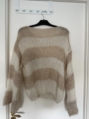 Beige och vit randig stickad tröja - Mysig stickad tröja med breda beige och vita ränder. Tröjan har en lös passform med låna vida armar. Säljer för den inte kommit till användning och används fåtal gånger. Tröjan är från design by si🥰