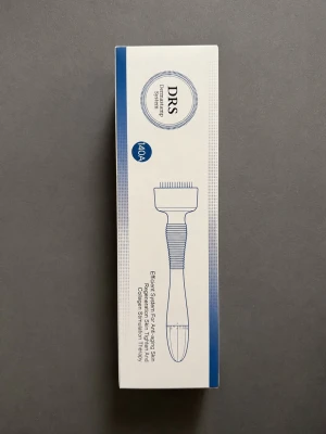 DRS Derma Roller System 140A - DRS Derma Roller System 140A är ett verktyg för microneedling och kollagenstimulering. Förpackningen är vit med blå detaljer och visar en illustration av verktyget som har ett greppvänligt handtag och en roller med små nålar. Perfekt för hudvård och anti-age behandlingar.