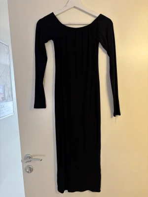 Svart ribbad långklänning - Snygg svart långklänning med ribbad struktur och lång ärm. Klänningen har en bred, rundad urringning och är figurnära i modellen. Perfekt för dig som gillar stilrena och enkla plagg med en modern touch. Man kan ha den off-shoulder.