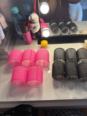 Papiljotter för håret i rosa och svart - Säljer ett set med hårspolar i två färger: sex stycken rosa och sex stycken svarta. Rullarna är stora och har kardborre för att enkelt fästa i håret. Perfekta för att skapa volym och lockar utan värme. Materialet är plast och kardborre.