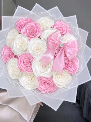 Bukett med rosa och vita rosor - Säljer en stor bukett med konstgjorda rosor i rosa och vitt, inslagen i vitt papper och dekorerad med en bred rosa sidenrosett. Perfekt som present eller dekoration. Blommorna är arrangerade i ett runt mönster och buketten har pärldetaljer runt kanterna.🌸✨