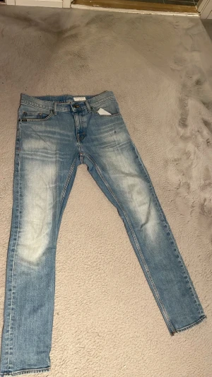 Ljusblå slim fit jeans - Säljer ett par ljusblå slim fit jeans med snygga slitningar och tvättade detaljer på låren och knäna. Klassisk femficksmodell med dragkedjegylf och smal passform. Perfekta till en avslappnad streetstyle-look.