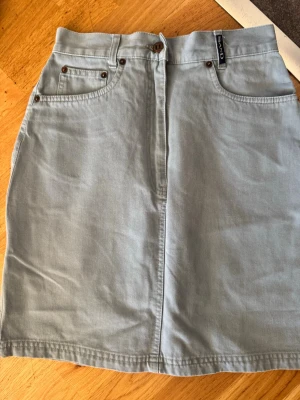 Ljusblå jeanskjol från SAND - Snygg ljusblå jeanskjol från SAND med klassisk femficksdesign, bälteshällor och knappstängning framtill. Kjolen har en rak passform och är tillverkad i mjuk bomull, perfekt för en avslappnad och trendig look.