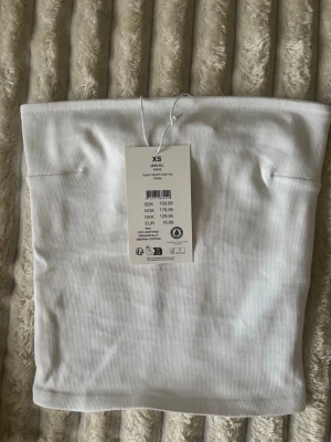 Vit ribbad tubtop - Säljer en vit ribbad tubtop i superstretchigt material. Toppen är axelbandslös och har en enkel, clean look som passar perfekt till jeans eller kjol. Tillverkad av ekologisk bomull för en mjuk och bekväm känsla.
