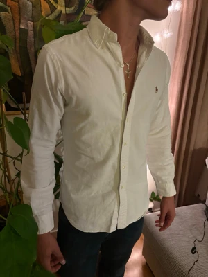 Ralph Lauren  - Klassisk vit skjorta med knappkrage och långa ärmar. Skjortan har en broderad logga på bröstet och stängs med knappar framtill. Tillverkad i bomull för en bekväm känsla och stilren look. Perfekt till jeans eller chinos. Storlek s