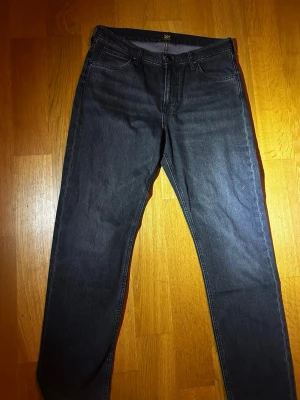 Svarta raka jeans från Lee W30 L32 - Snygga svartgrå jeans från Lee med klassisk rak passform och fem fickor. Jeansen har en enkel design med subtila sömmar och är tillverkade i slitstarkt denimtyg. Perfekta för en clean och stilren look.
