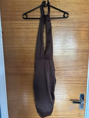 Brun halterneck baddräkt - Snygg brun baddräkt med halterneck och djup urringning. Modellen har breda axelband som knyts i nacken och en enkel, stilren design. Materialet är troligtvis stretchigt och snabbtorkande, perfekt för strand eller pool.
