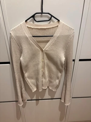 Beige ribbad kofta från SHEIN - Snygg beige ribbad kofta från SHEIN med v-ringning och tre knappar framtill. Långärmad modell i mjukt material med lätt stretch. Perfekt att slänga över en topp eller klänning för en chill look.