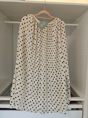 Vit plisserad prickig långkjol - Säljer en vit långkjol med svarta prickar och plisserad design. Kjolen har en luftig och flowy känsla, perfekt för dig som gillar en lekfull och trendig stil. Resår i midjan för skön passform.