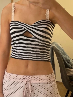 Randig croppad topp från Bershka - Säljer en svartvit randig croppad topp från Bershka med twistad front och cut-out detalj under bysten. Toppen har smala axelband och är perfekt för dig som gillar trendiga och unika plagg. Materialet är mjukt och stretchigt, troligen bomull eller polyester.